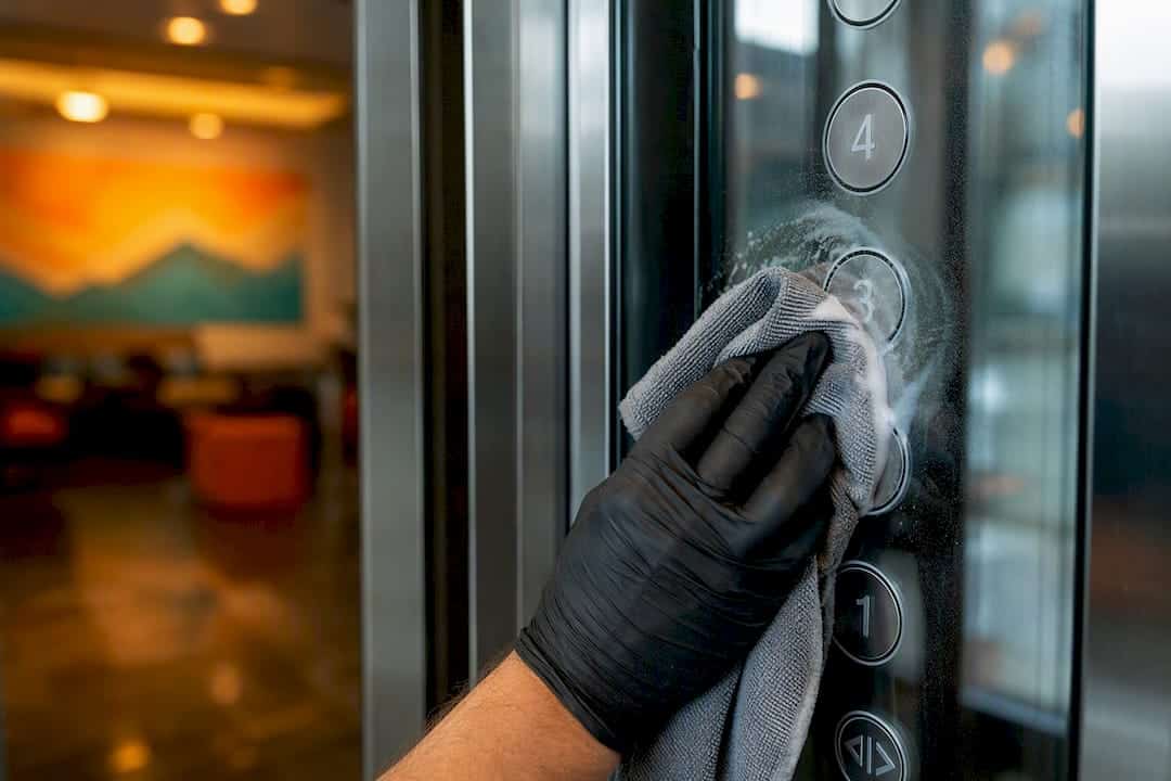 Gloved hand cleaning elevator buttons