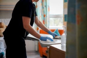 Gloved hands disinfecting hospital bed rail