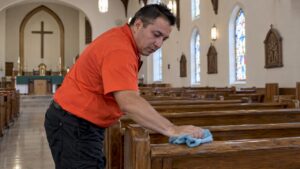 Custodian wiping a wooden church pew rail